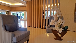 A lobby with a grey armchair, a round table with a vase of white flowers, and a wooden partition. - Shell Residences Apartment by Homebound (Pasay)