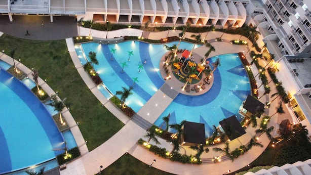 A multi-level hotel with a central swimming pool surrounded by palm trees and lounge areas. - Shell Residences Apartment by Homebound (Pasay)