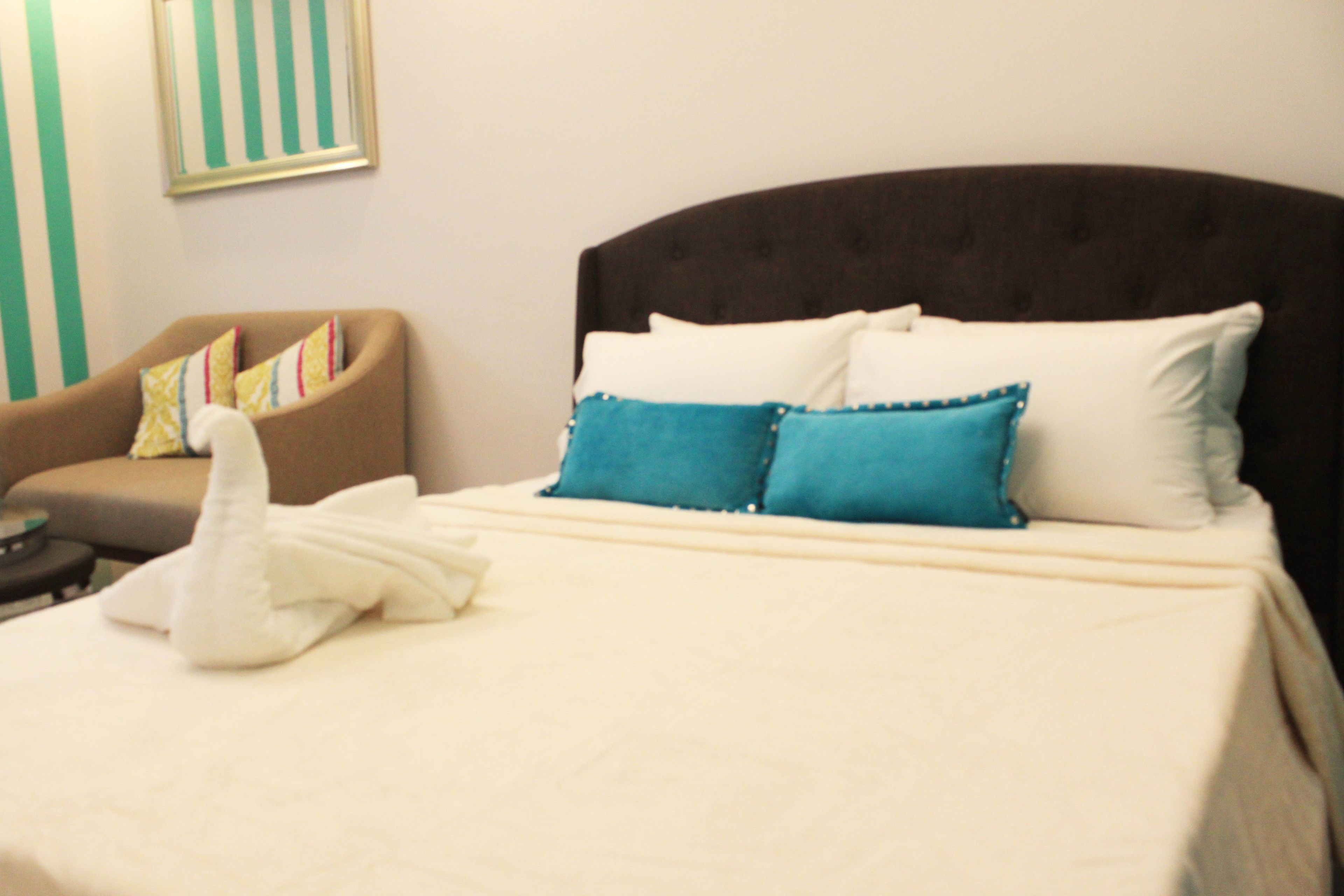 A hotel room with a bed, a brown armchair, and a white towel on the bed.