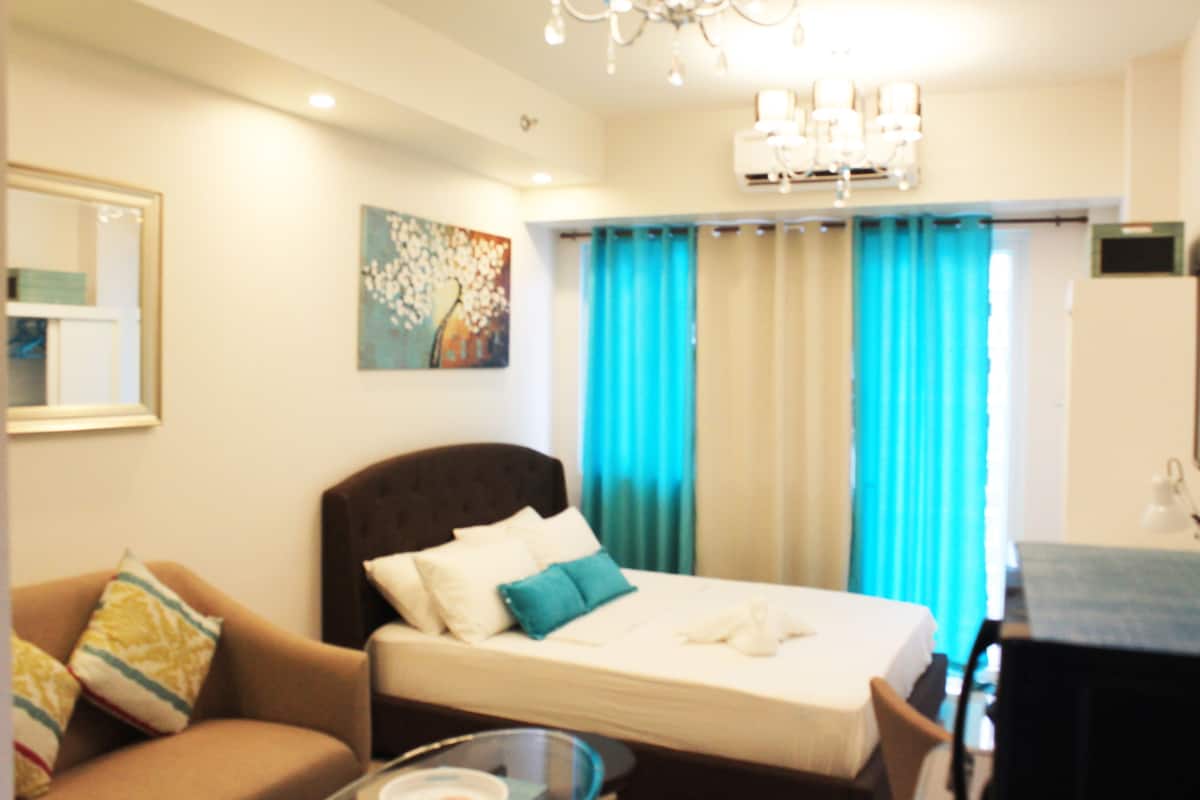 A hotel room with a bed, a sofa, a glass coffee table, and a dining area.