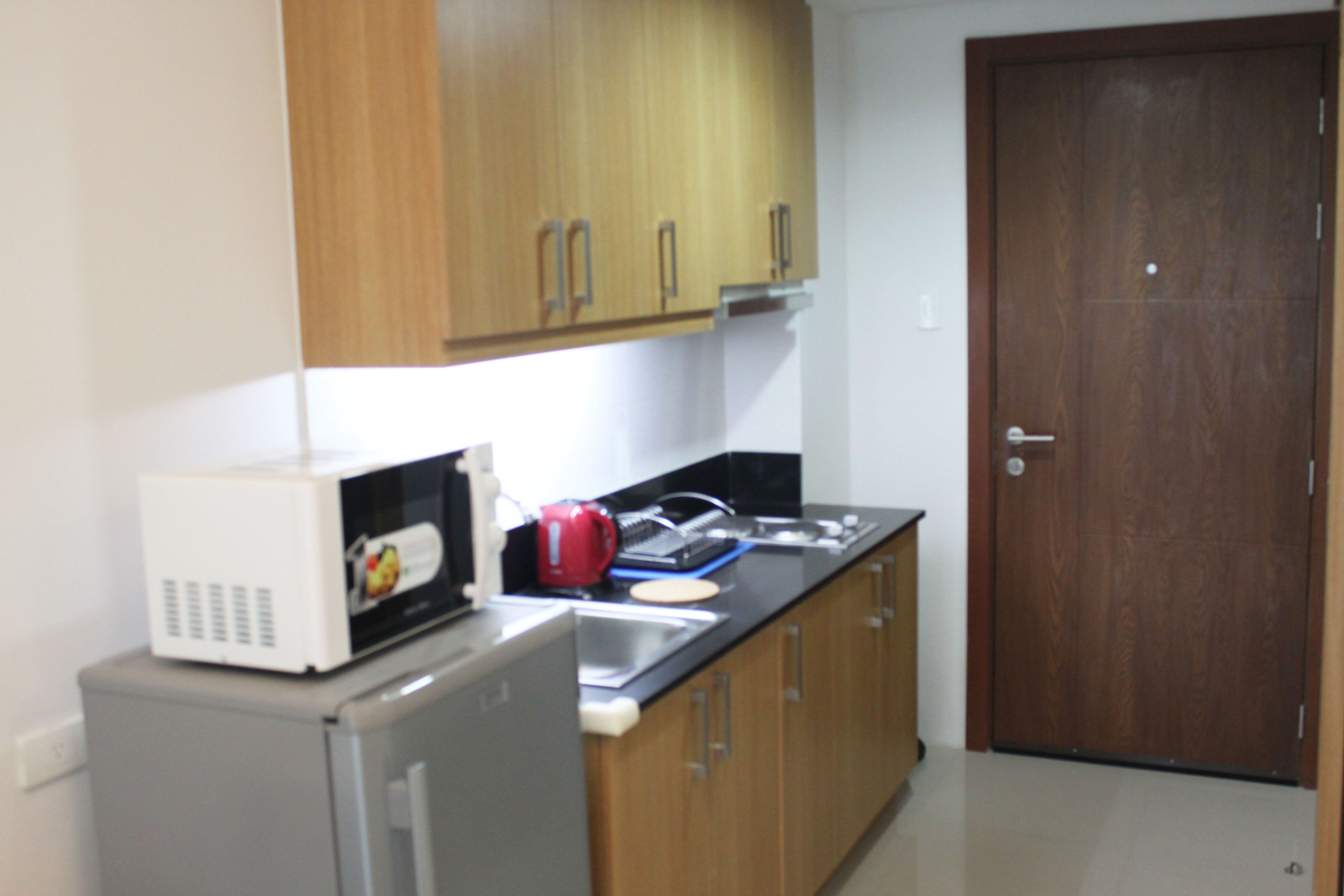 A kitchen with wooden cabinets, a microwave, a kettle, and a sink.
