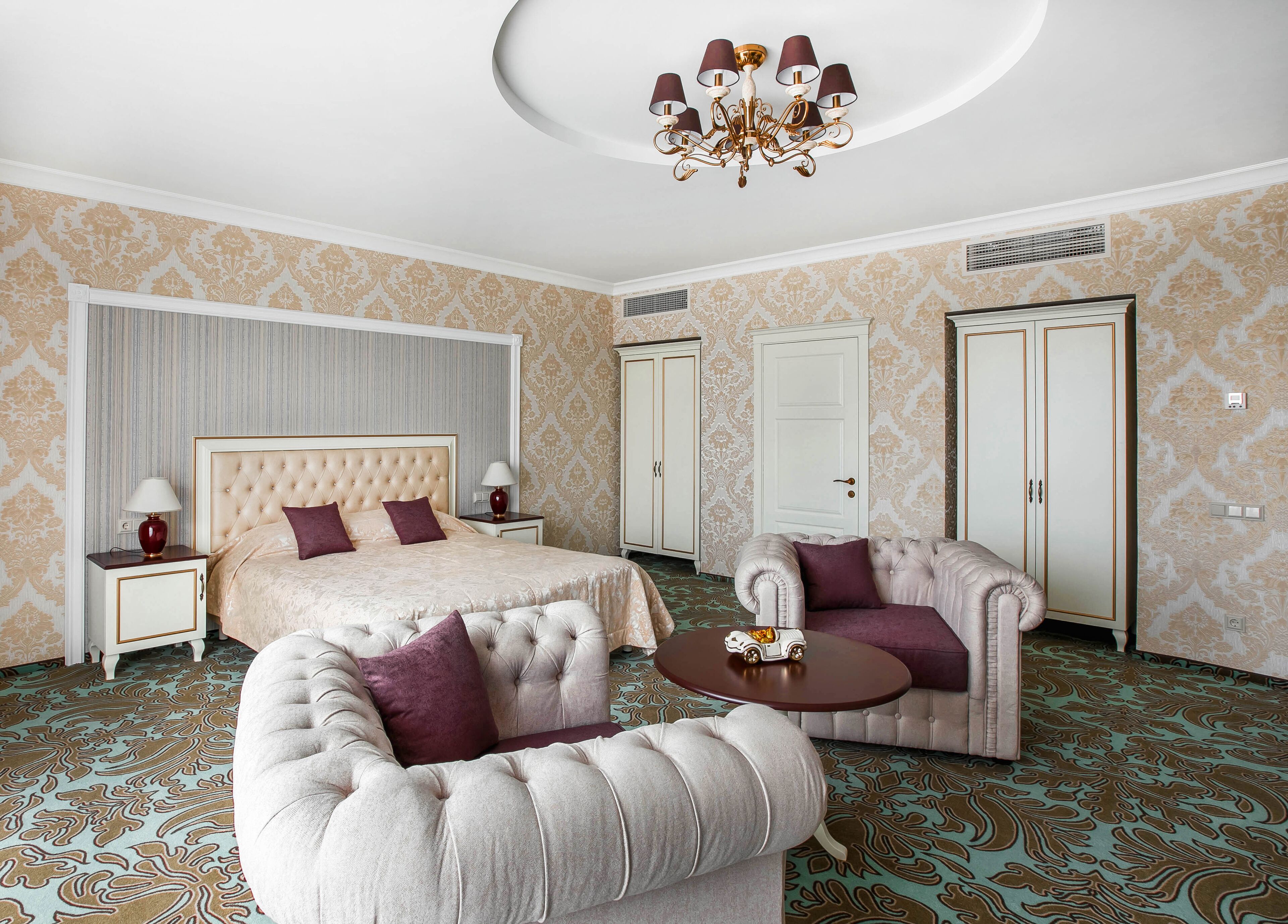 Ein Hotelzimmer mit einem großen Bett, zwei Sesseln, einem kleinen Tisch und einer Kristallleuchter.