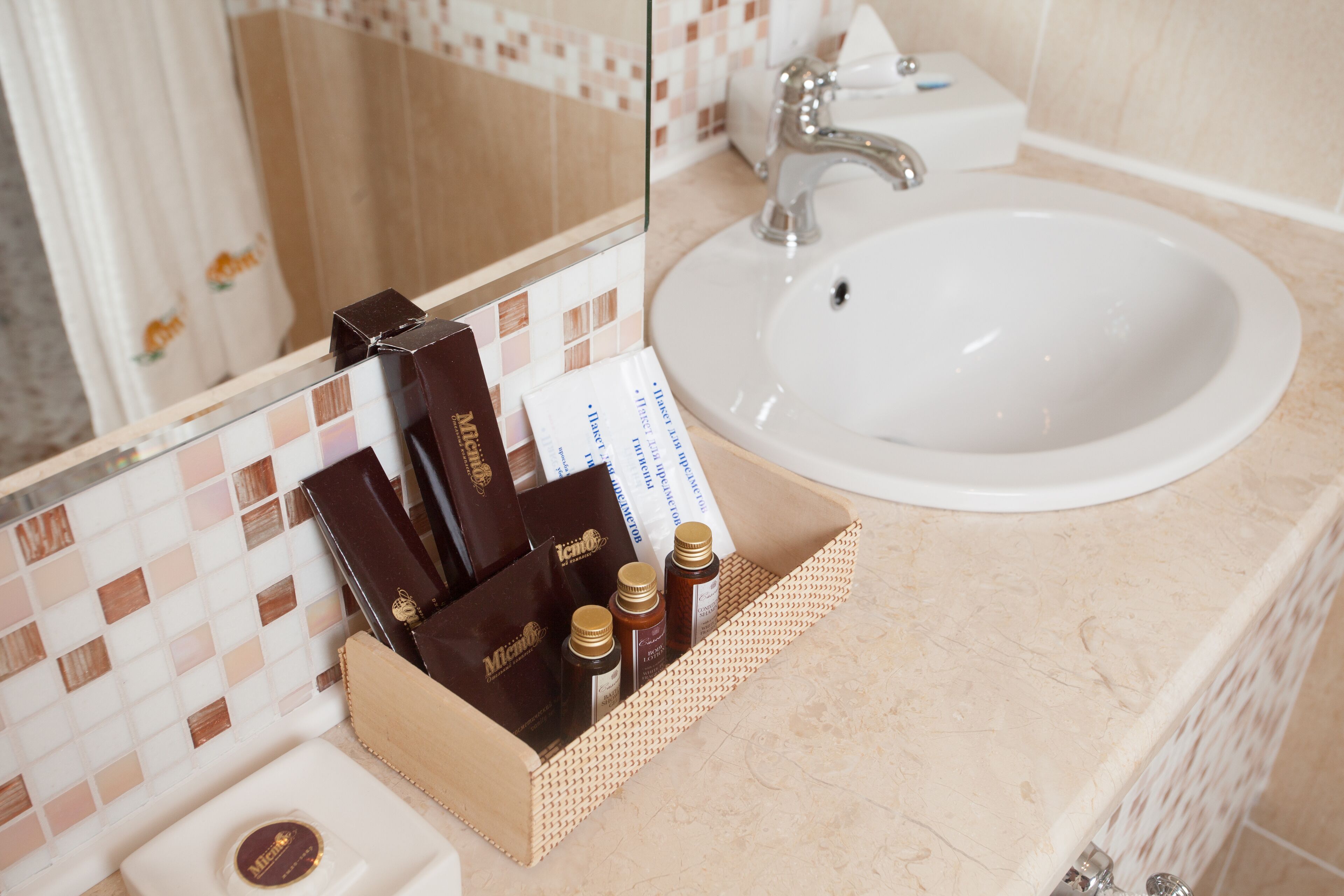 A bathroom with a white sink, a mirror, and toiletries in a basket.