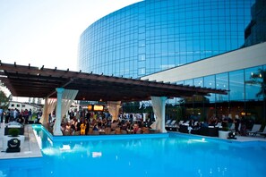 A pool area with lounge chairs and a covered seating area, adjacent to a modern building with reflective glass windows. - Hotel Complex Misto (Kharkiv)