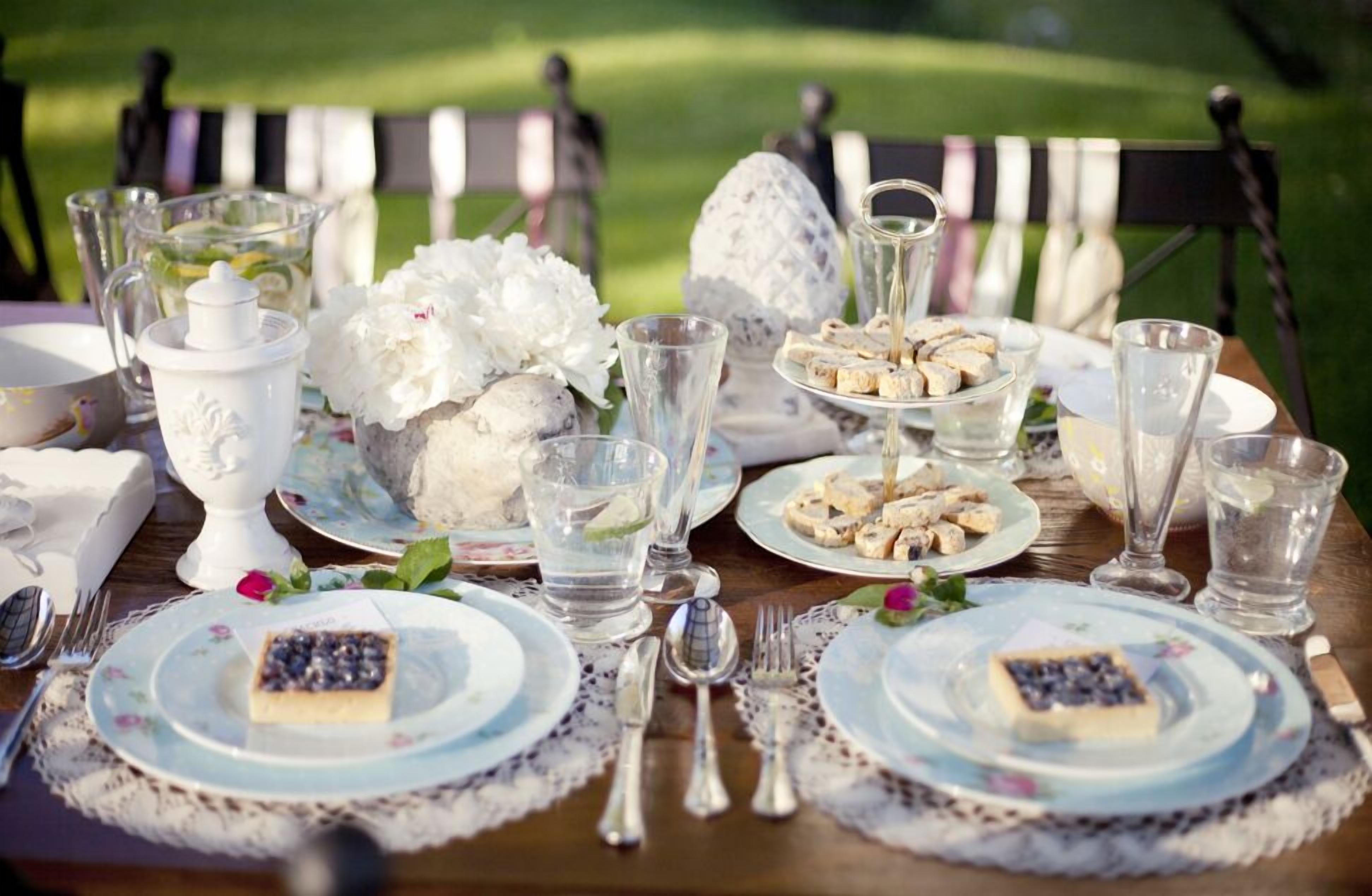 A table set for a meal with plates, cutlery, and glasses, surrounded by decorative elements and a view of a green landscape.