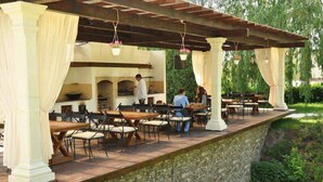 Une terrasse extérieure avec des tables et des chaises, un mur en pierre et une structure en forme de pergola.