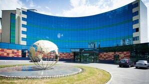 Un bâtiment moderne doté d’une façade en verre incurvée, d’une sculpture sphérique centrale et d’un espace de stationnement avec des voitures.