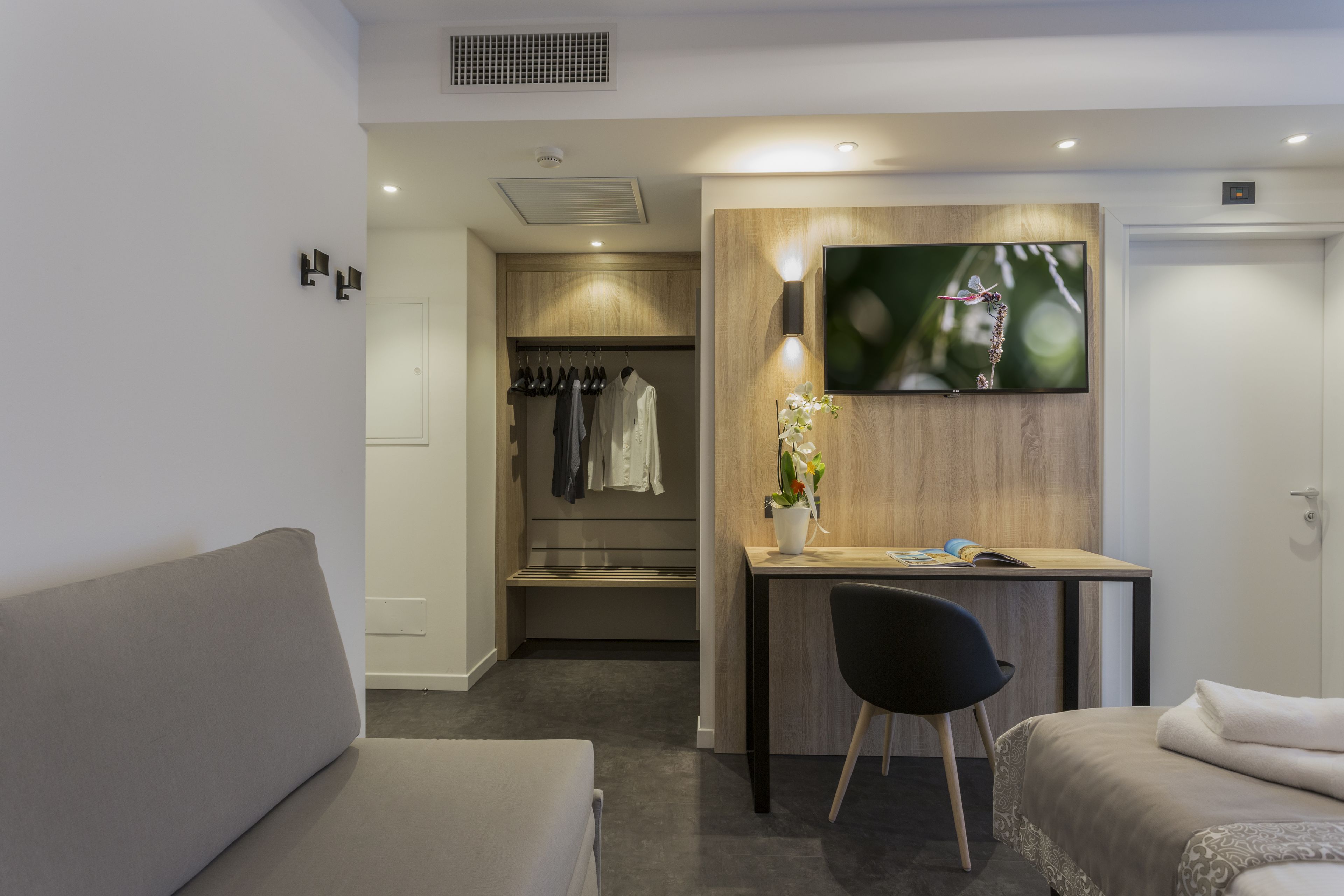 Ein modernes Hotelzimmer mit einer Couch, einem Bett, einem Schreibtisch mit Stuhl, einem Kleiderschrank und einem an der Wand befestigten Fernseher.