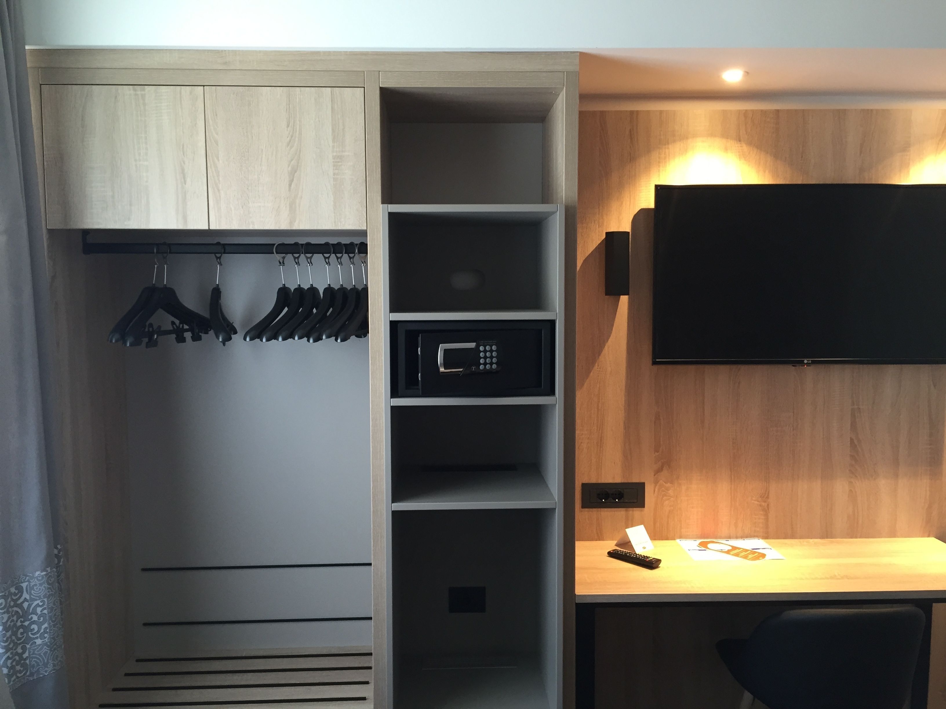 A modern room with a built-in wardrobe, a desk with a flat-screen TV, and a microwave.