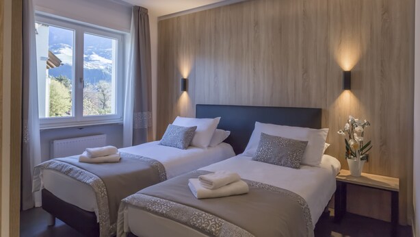 Camera d'albergo con due letti, vista sulle montagne attraverso una finestra e un pannello di parete in legno.