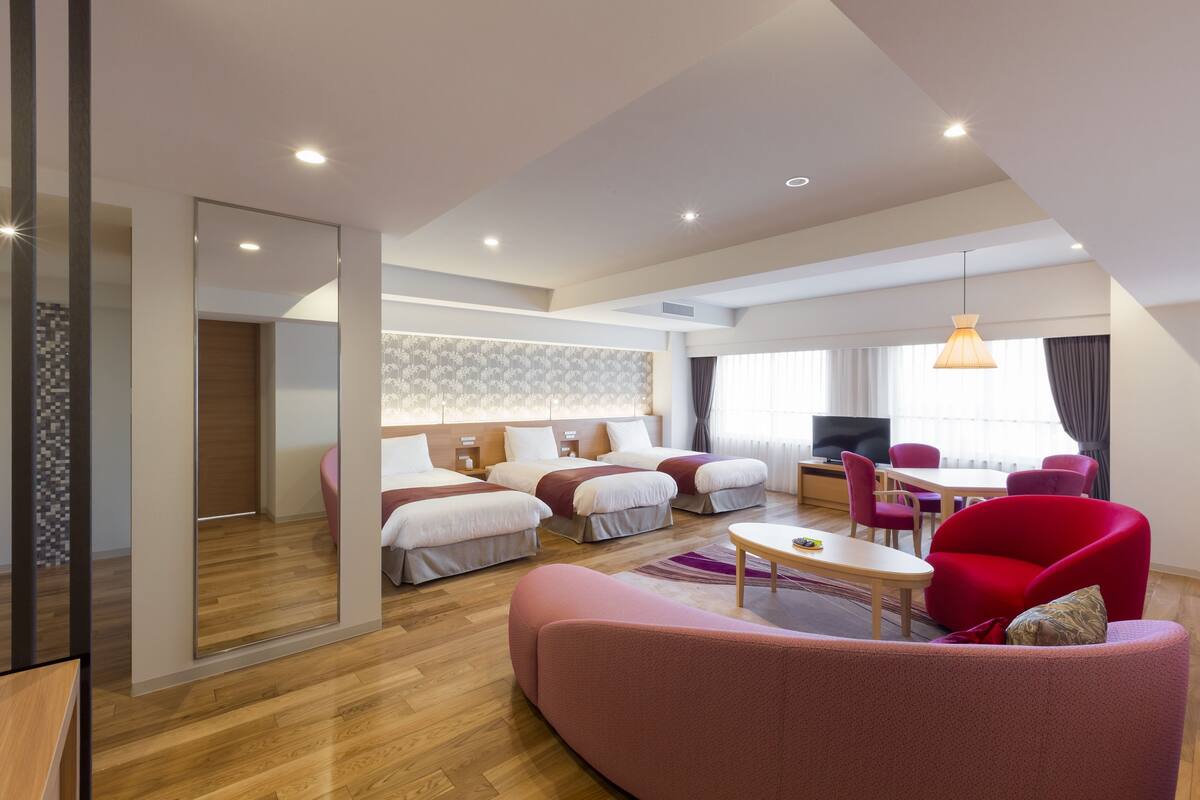 Una habitación de hotel moderna con una cama grande, un sofá, una mesa de comedor y un televisor.