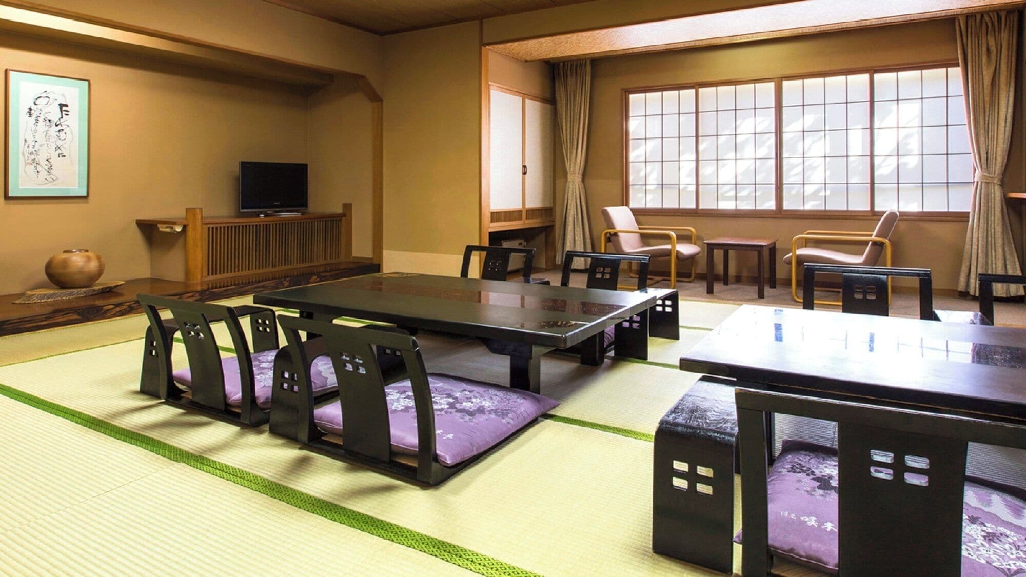 A traditional Japanese room with tatami flooring, a low table, chairs, a television, and a window with curtains.
