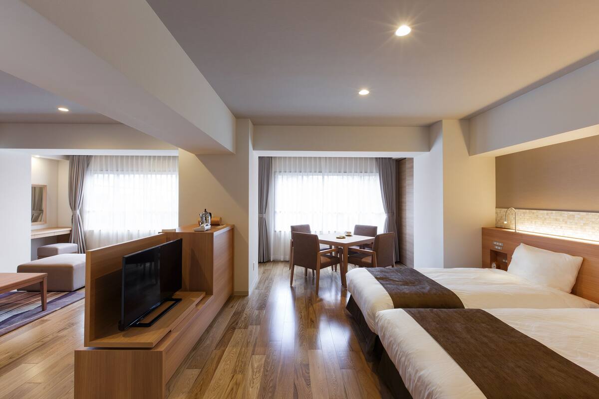 Habitación de hotel con televisión de pantalla plana, una mesa de comedor con sillas, una cama y una mesita de noche.