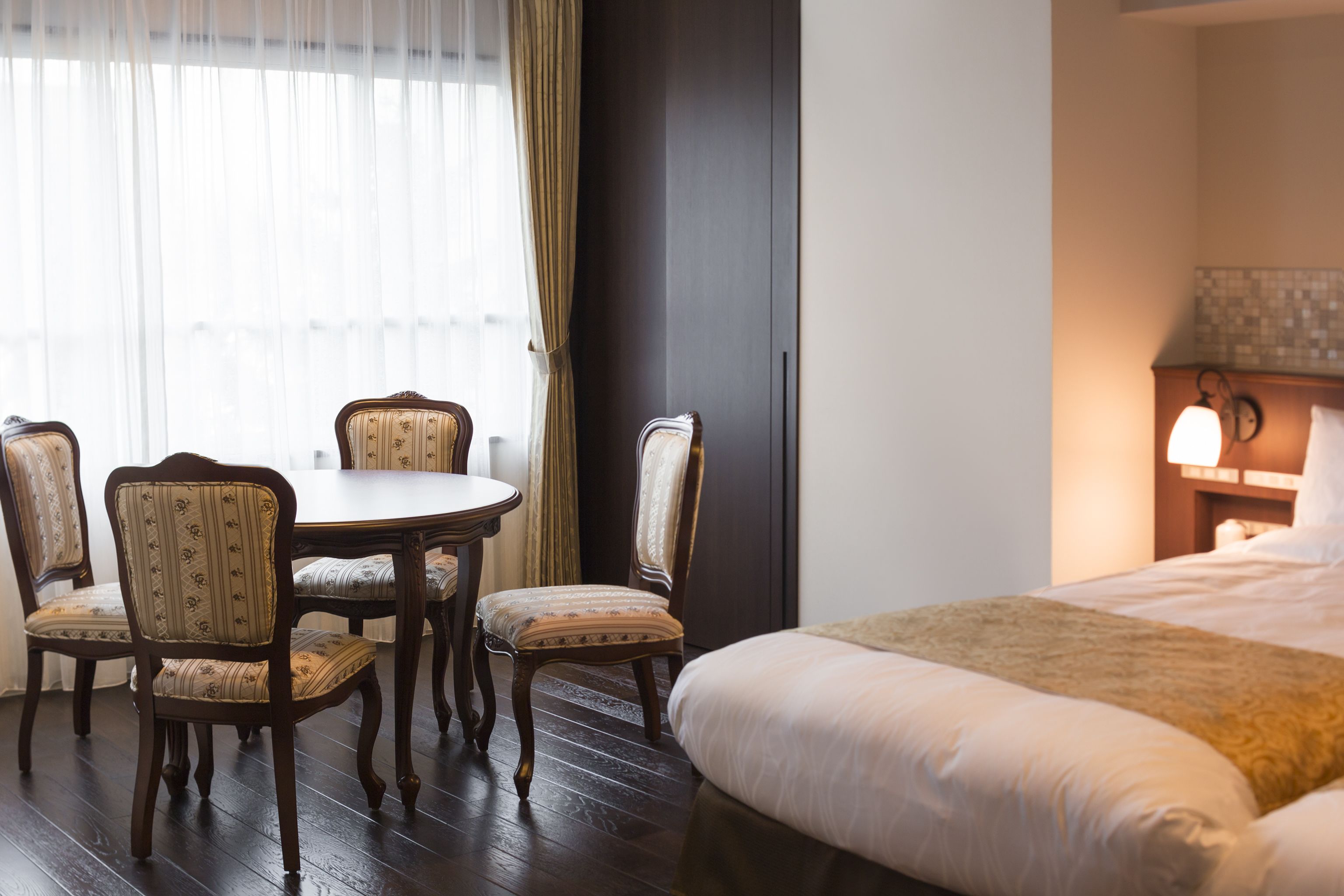 A hotel room with a bed, a round table with four chairs, and a nightstand with a lamp.