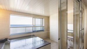 Un baño moderno con cabina de ducha de vidrio, bañera y un amplio ventanal con vistas al mar.