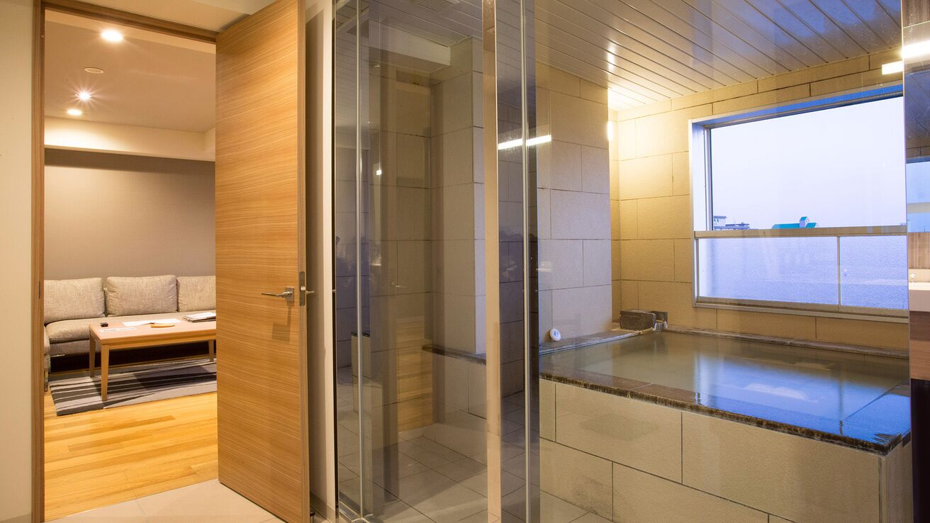 A modern bathroom with a glass shower enclosure, a wooden vanity, and a view of the city through a large window.