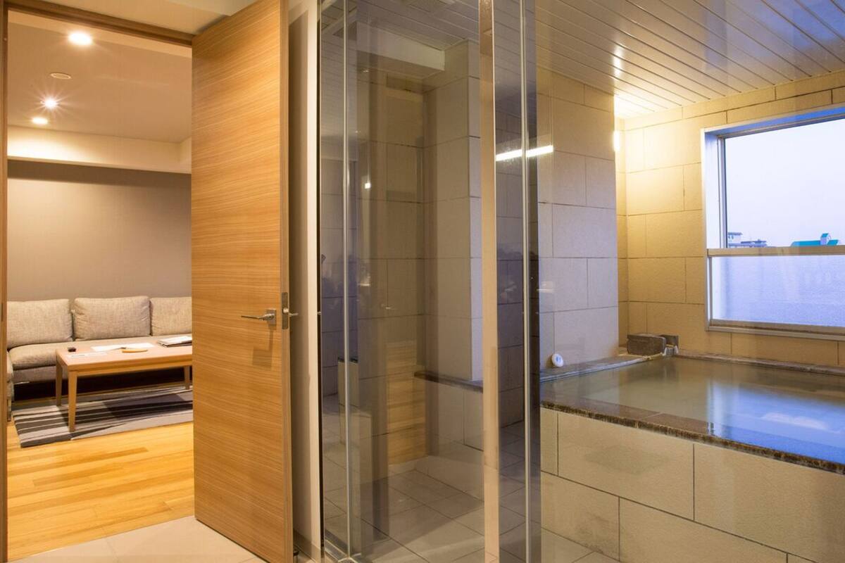 Un baño moderno con cabina de ducha de vidrio, tocador de madera y vistas a la ciudad a través de un ventanal amplio.
