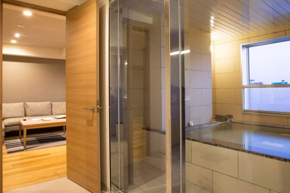 A modern bathroom with a glass shower enclosure, a wooden vanity, and a view of the city through a large window.
