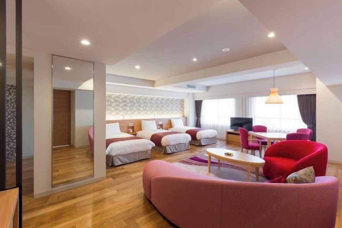 Una habitación de hotel moderna con suelo de madera, un sofá, una mesa de comedor y un televisor.