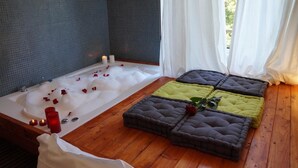 A spa room with a large bathtub, wooden flooring, and two cushioned seating areas. - Jacuzzi Rooms (Rome)