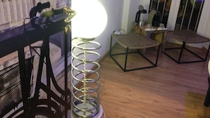 A room with a wooden floor, a wicker chair, a metal-framed table, and a lamp with a round shade. - Jacuzzi Rooms (Rome)