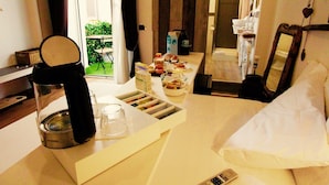 A hotel room with a bed, a bedside table with a coffee maker, a glass of water, a bowl of fruit, and a bathroom visible through an open door. - Jacuzzi Rooms (Rome)