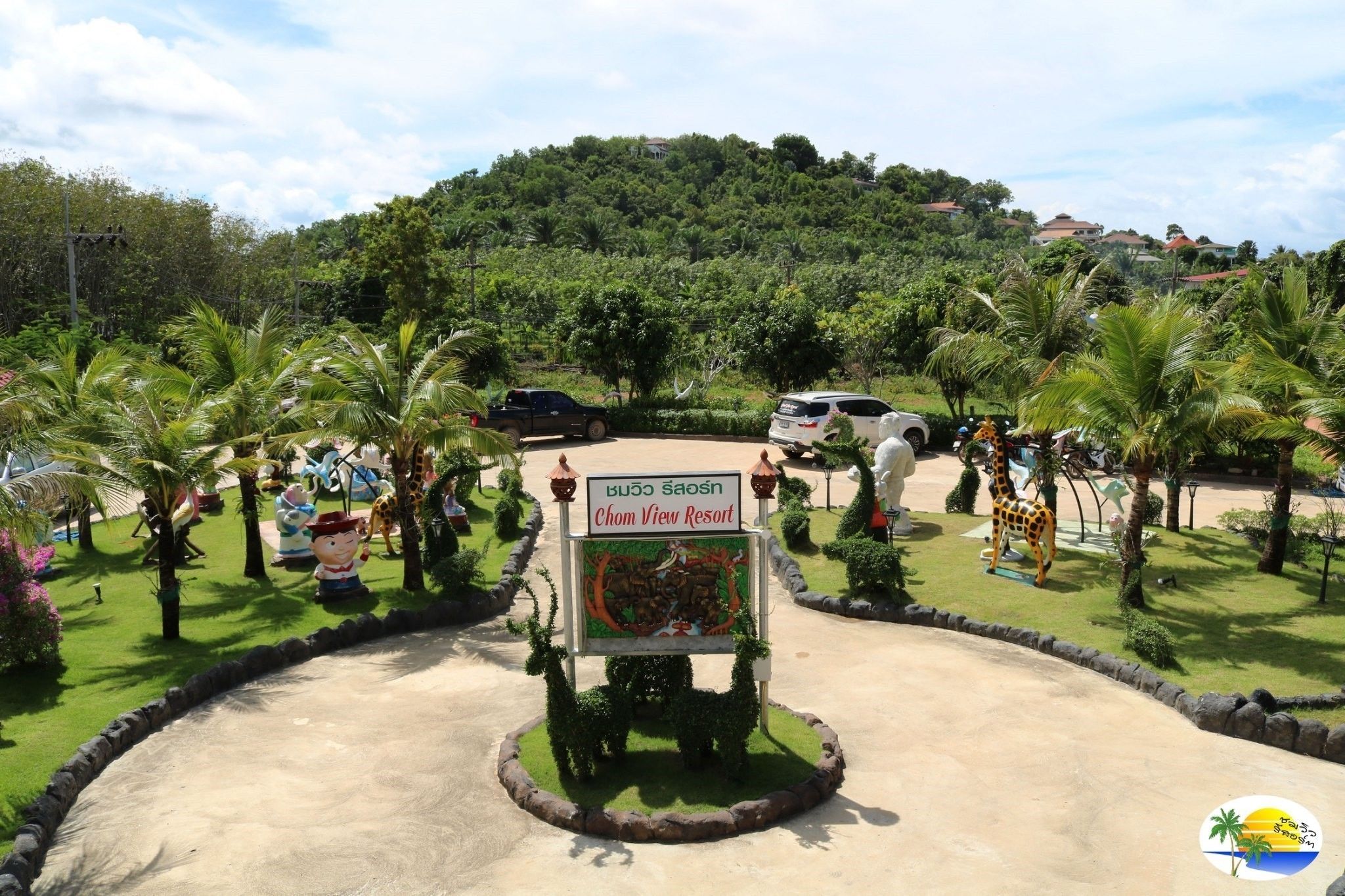 A sign for Chom View Resort surrounded by lush greenery and palm trees.
