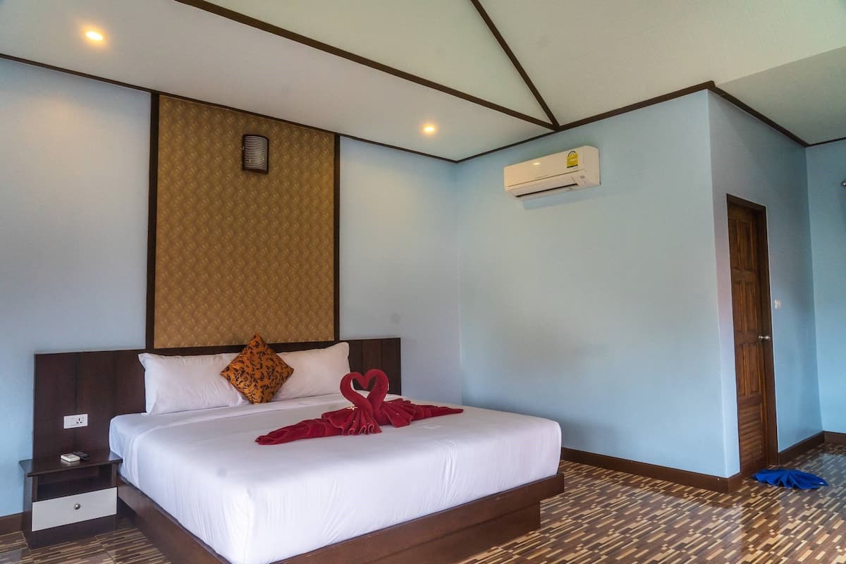 A hotel room with a neatly made bed, a wooden headboard, a wall-mounted air conditioner, and a patterned carpet.
