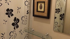 Casa de banho com sanita, prateleira de vidro, decoração de folha emoldurada e espelho.