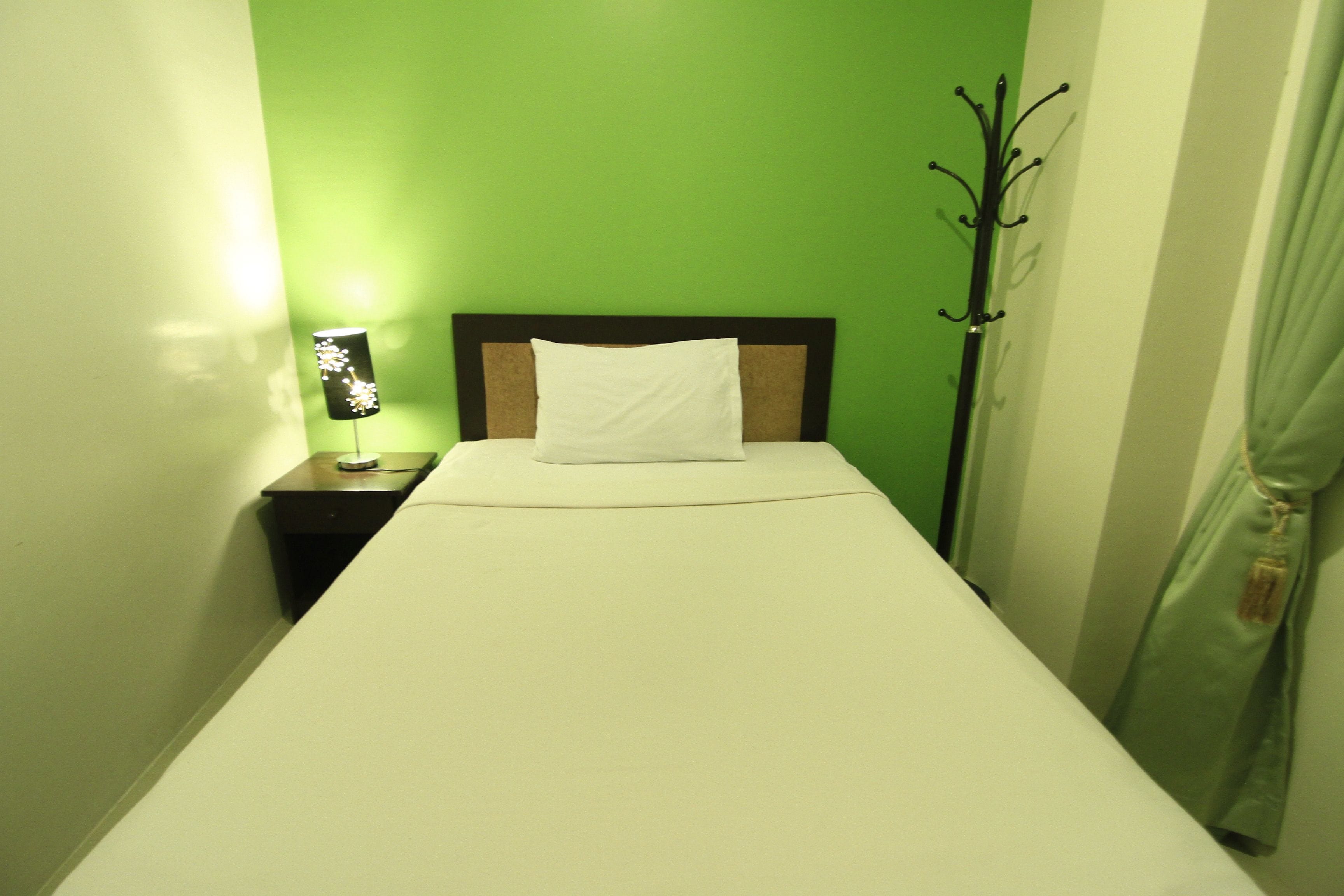 A single bed with white bedding in a room with green walls.