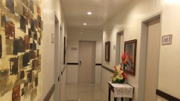 Um corredor com piso polido, parede com padrão em mosaico, mesa com arranjo floral e portas com a inscrição 