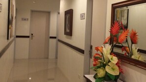 Um corredor de hotel com piso polido, uma recepção com um vaso de flores e portas com a inscrição 'Unidade 5' e 'Unidade 7'.