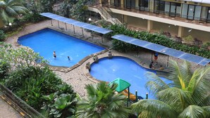 A swimming pool with a sunshade, surrounded by greenery and a building with balconies. - Literooms At Kebagusan City (Jakarta)