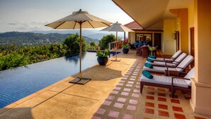 Una piscina infinita con vistas a las montañas, sillas de descanso y sombrillas.