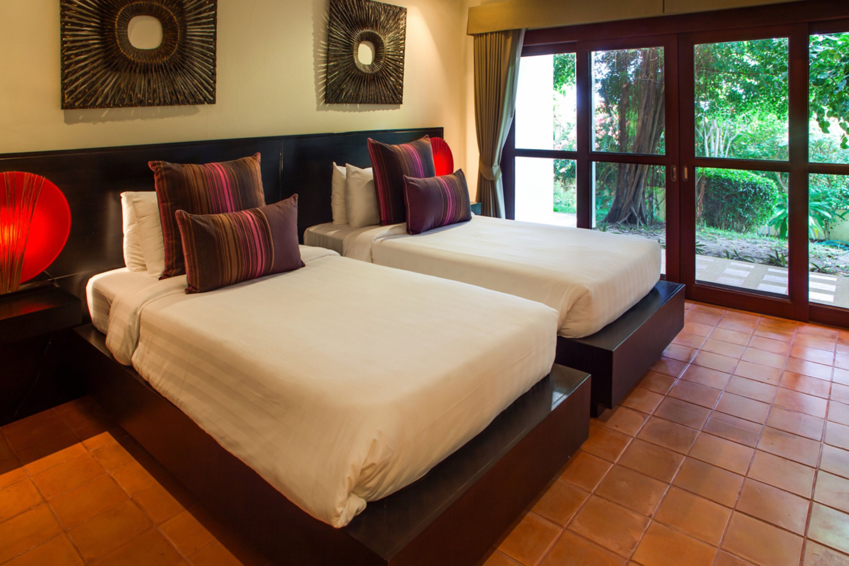 A hotel room with two beds, a large window with a view of greenery, and a decorative wall piece.