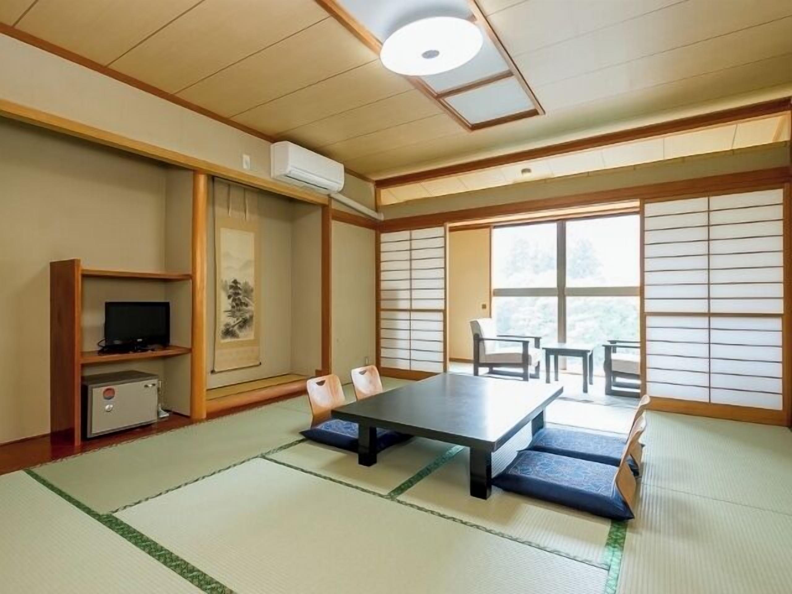 Quarto japonês tradicional com tatames, uma mesa baixa, cadeiras, televisão e aquecedor.