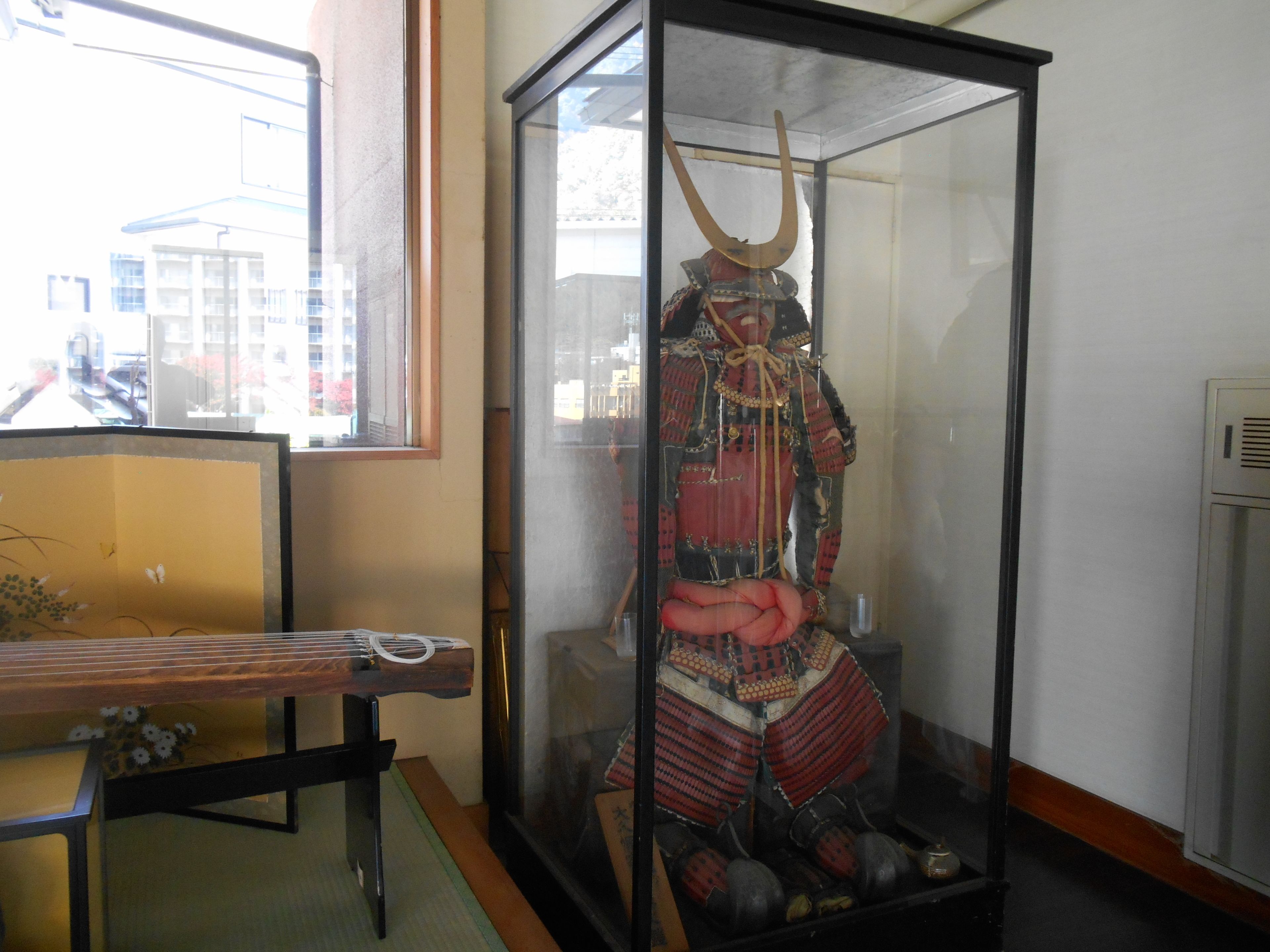 A display case containing a samurai armor with a helmet, chest plate, and leg guards.
