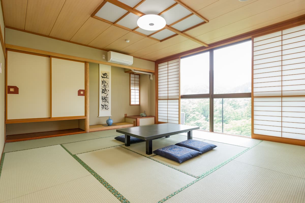 Ett traditionellt japanskt rum med tatamimattor på golvet, ett lågt bord, skjutdörrar och utsikt över grönskan.