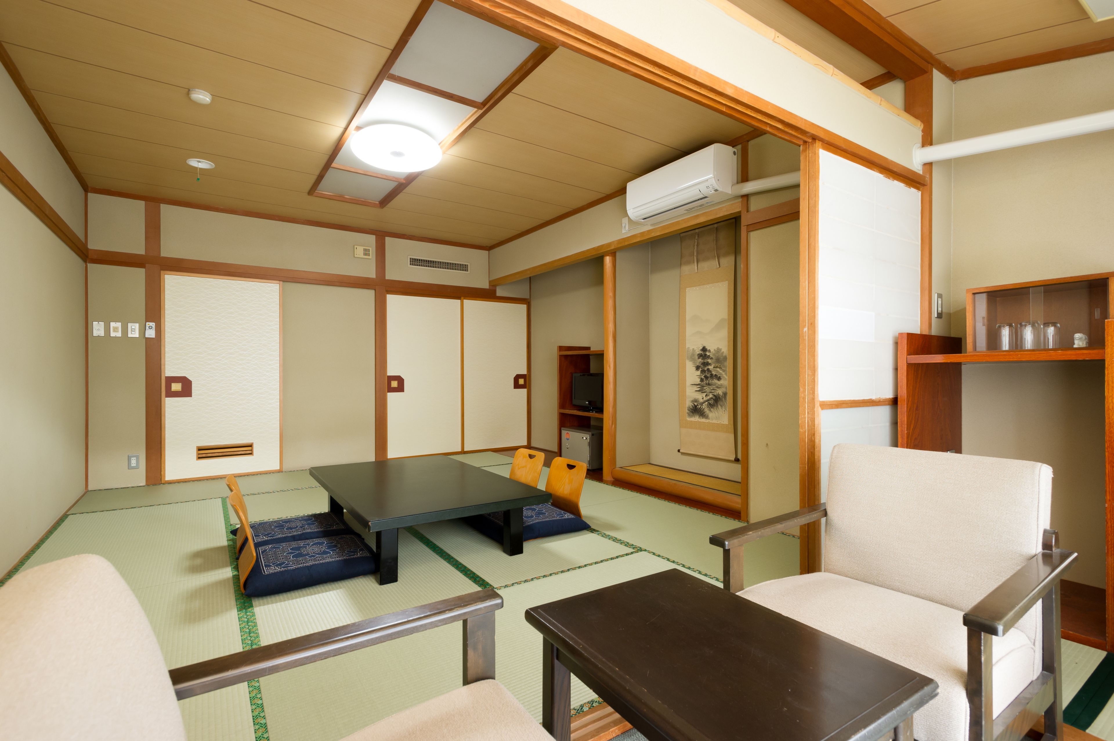 A traditional Japanese room with tatami flooring, a low table, a chair, and a shelf with glassware.