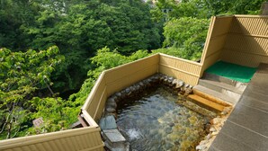 Une zone de sources chaudes avec des marches en pierre menant à une petite piscine, entourée de rampes en bois et d’une végétation luxuriante.