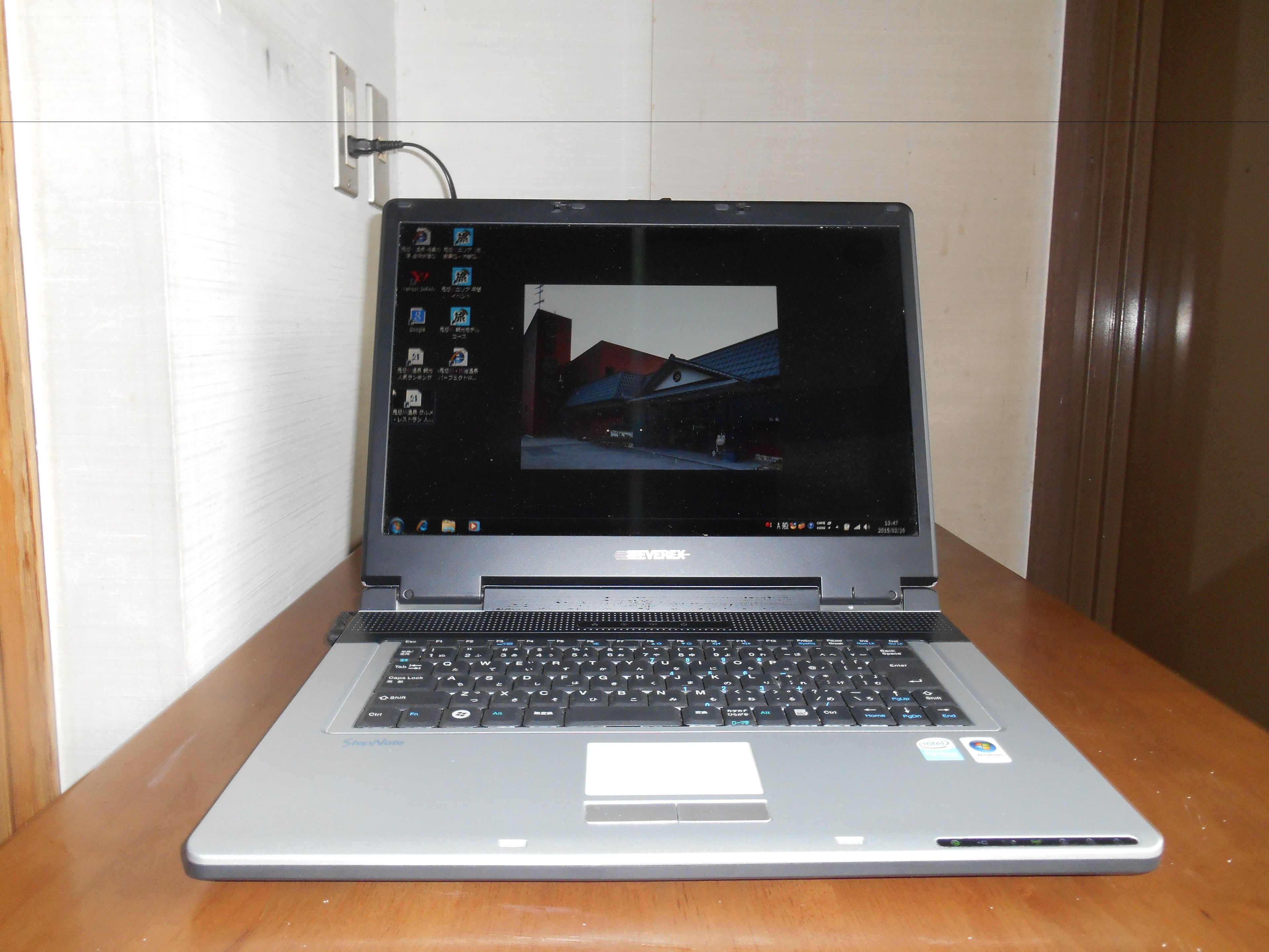 A laptop on a wooden table with a tiled wall in the background.