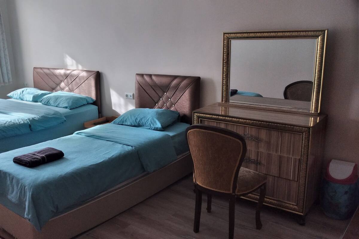 A hotel room with two beds, a wooden dresser with a mirror, and a chair.