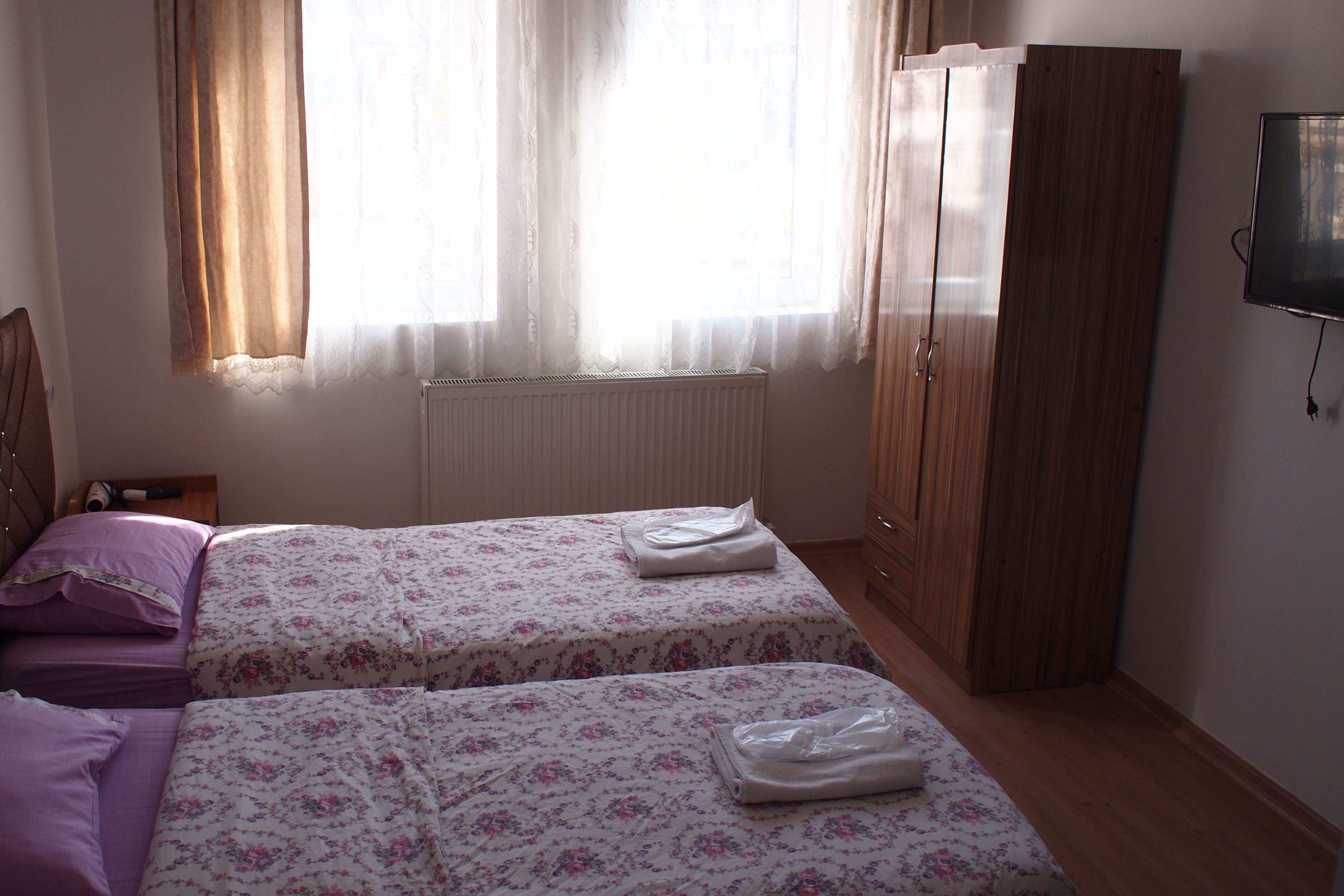 Ein Schlafzimmer mit zwei Betten, einem Kleiderschrank, einem Heizkörper und einem an der Wand montierten Fernseher.