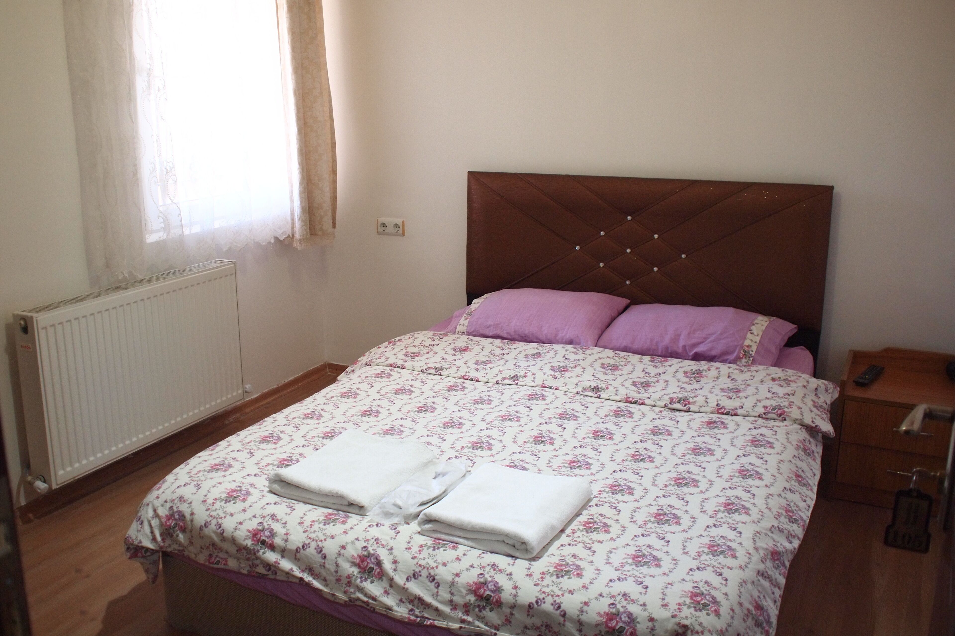 A bedroom with a bed, a radiator, a nightstand, and a window with curtains.