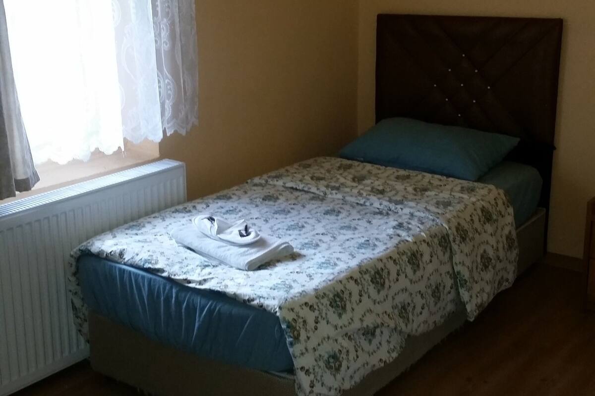 A single bed with a floral bedspread, a blue pillow, and a white towel on the footboard.