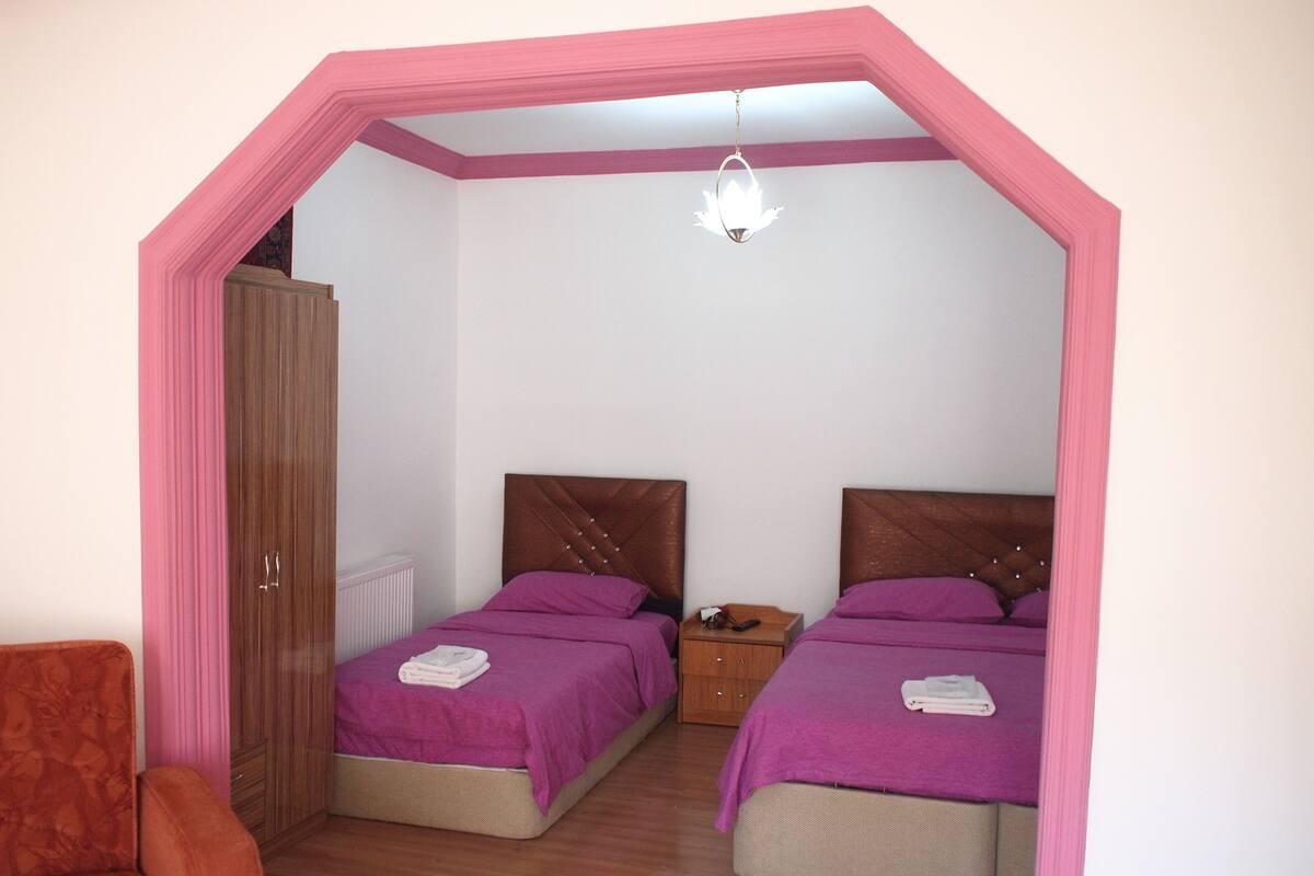 A bedroom with two beds, a wardrobe, a nightstand, and a hanging light fixture.