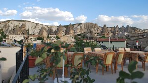 Eine Terrasse mit Sitzgelegenheiten im Freien, mit Blick auf eine Stadt und markante Felsformationen.