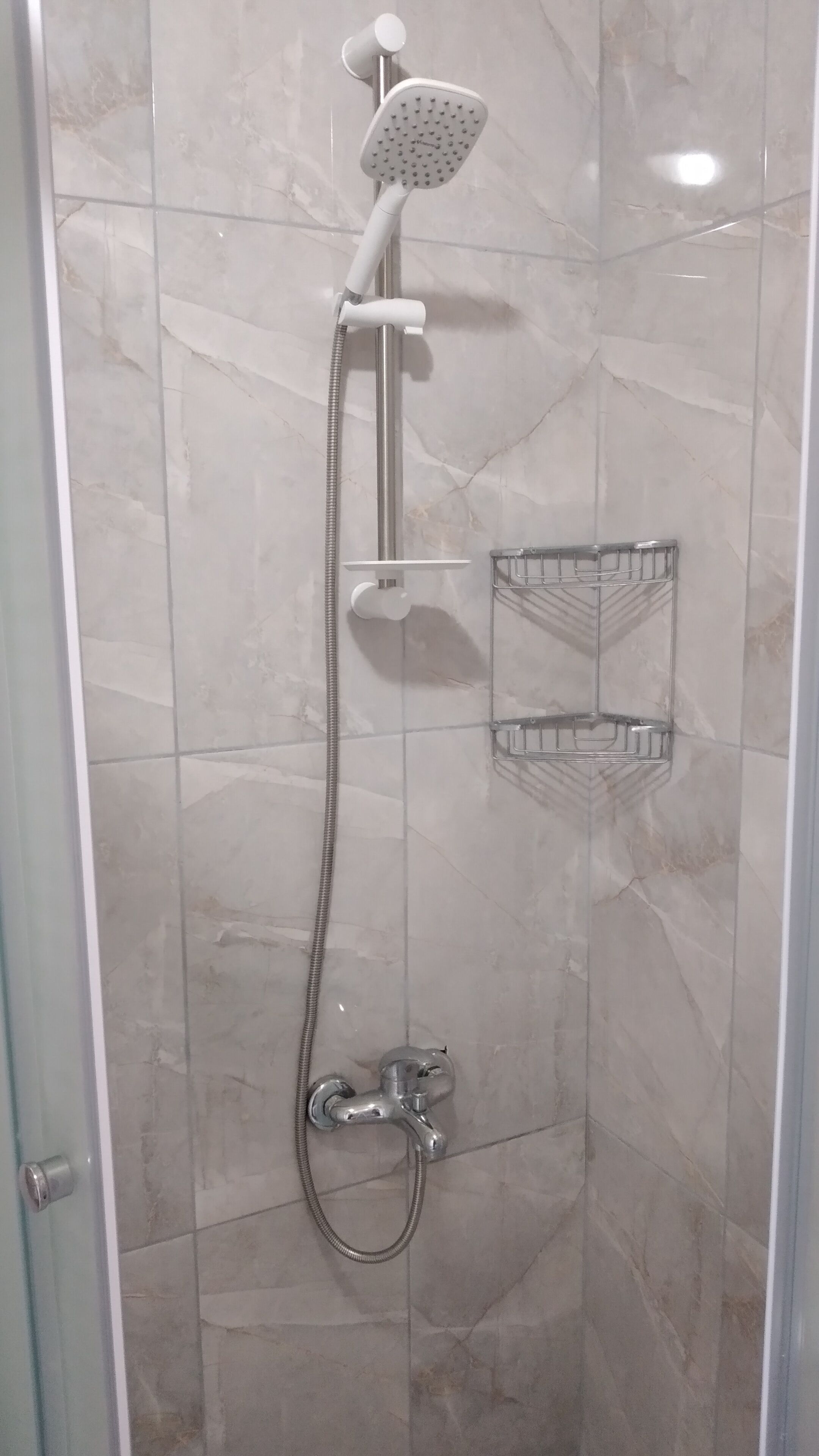 A shower enclosure with a handheld showerhead, a wall-mounted faucet, and a shower tray.