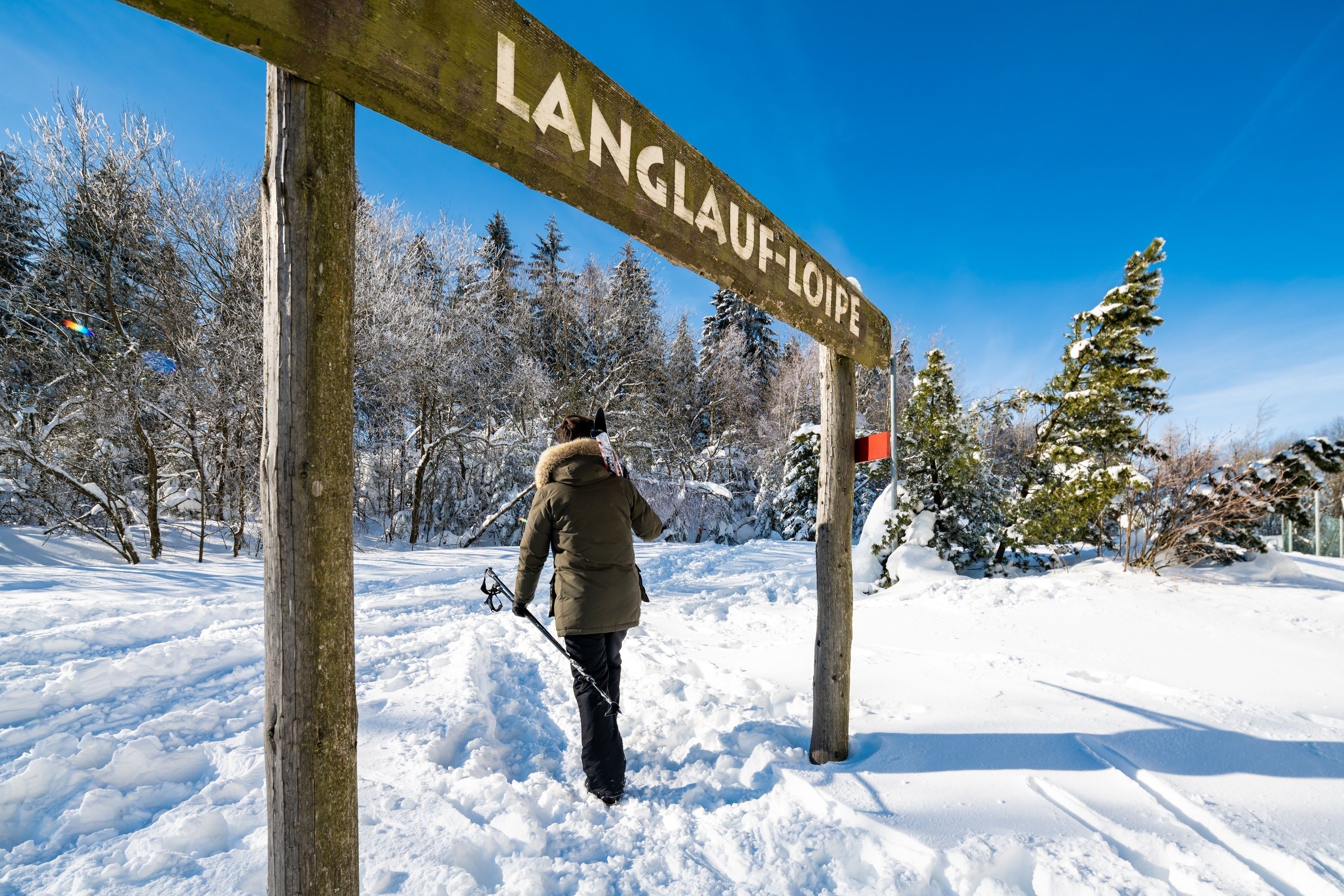 A wooden signpost with the text "LANGLOUF-LOIPE" in a snowy landscape.