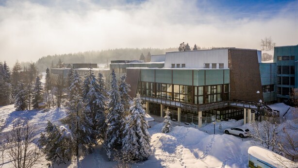 A modern building with large windows and a flat roof, surrounded by snow-covered trees and a clear sky. - AHORN Waldhotel Altenberg (Altenberg)